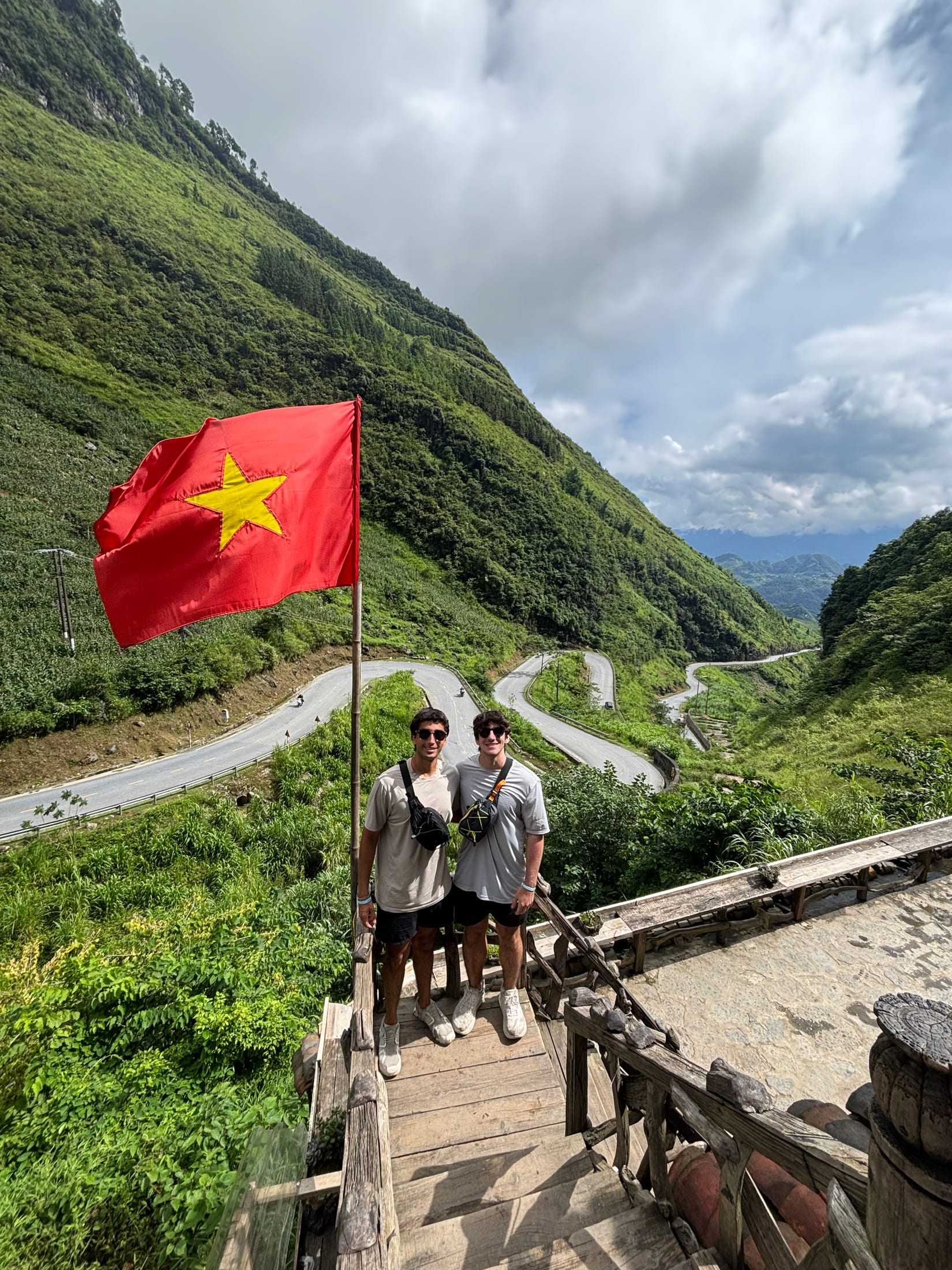 Standing with a friend beside a Vietnamese flag overlooking the mountain roads of Ha Giang